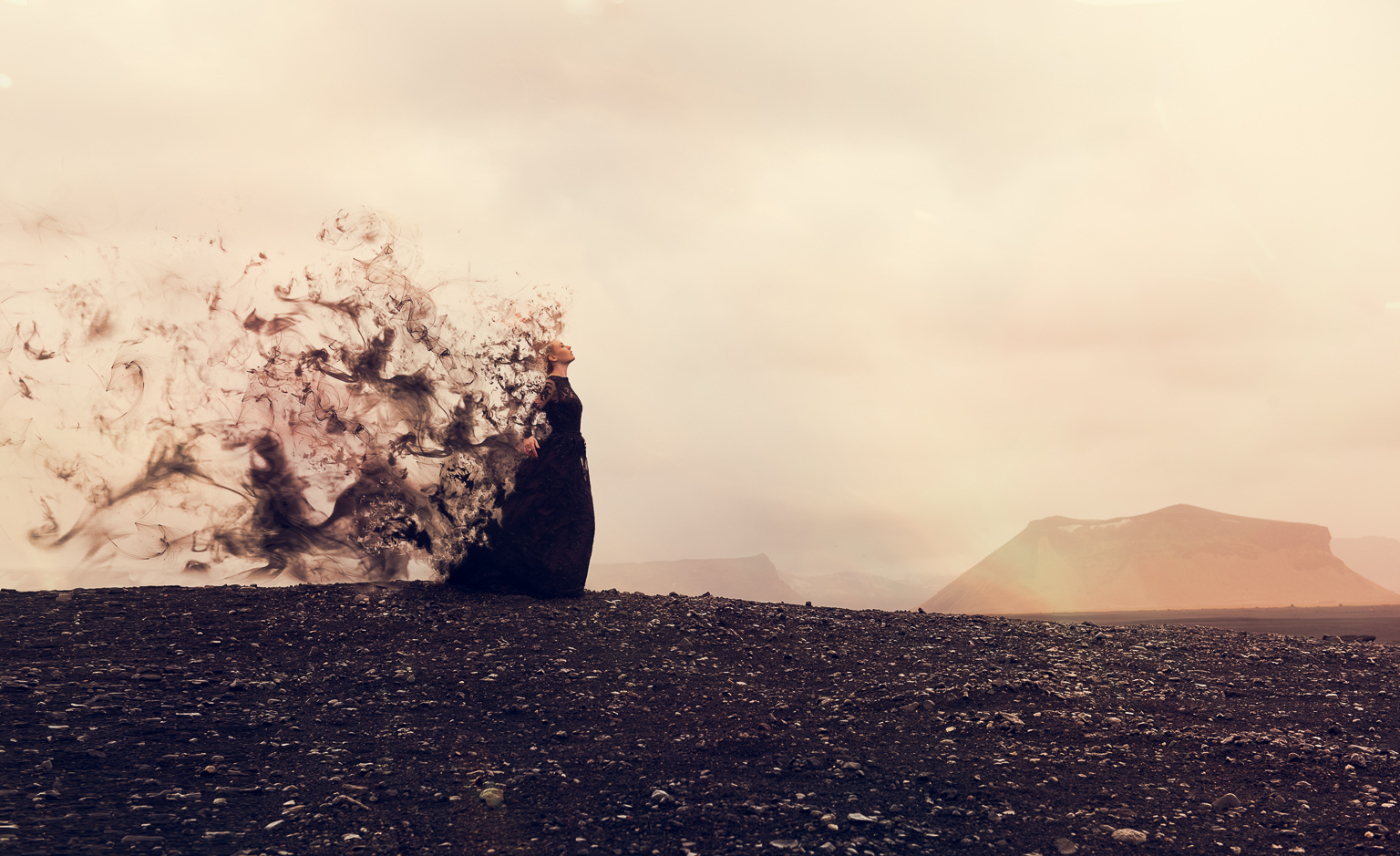 A model in a black dress on a black beach in Iceland. Orange sky and the dress is disintegrating into smoke behind her using photoshop. Taken and edited by Ian MEars
